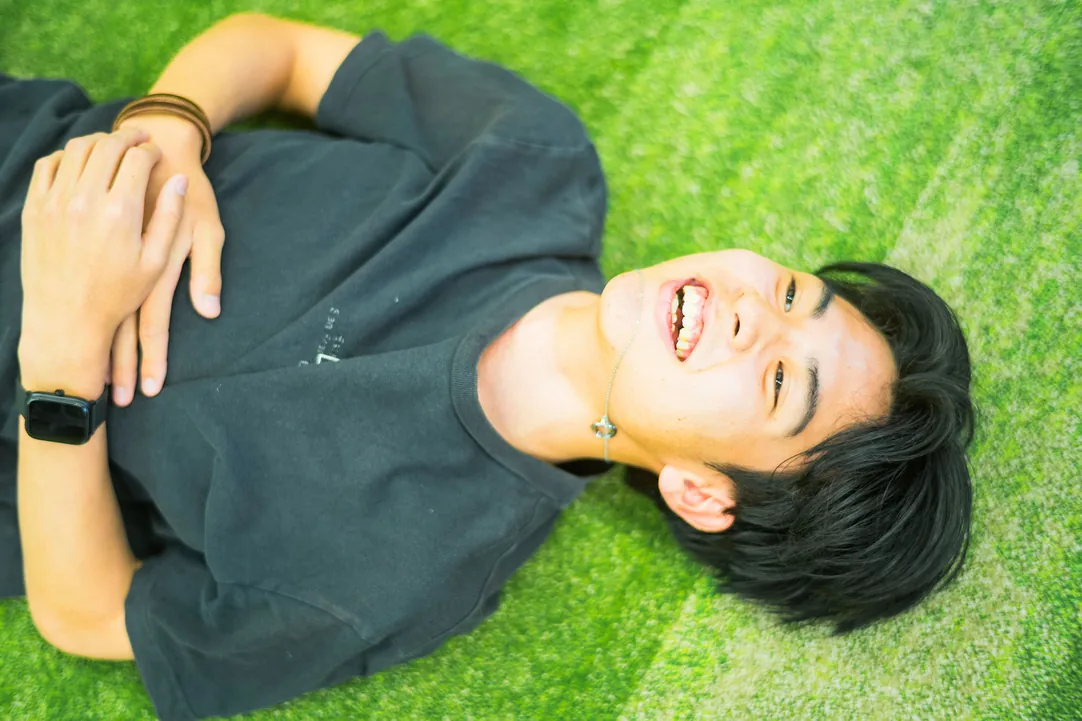 芝生の上で仰向けになり笑う男子生徒