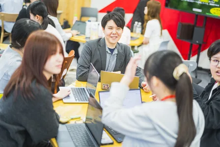 ノートPCを囲んで話し合う生徒たちとコーチ